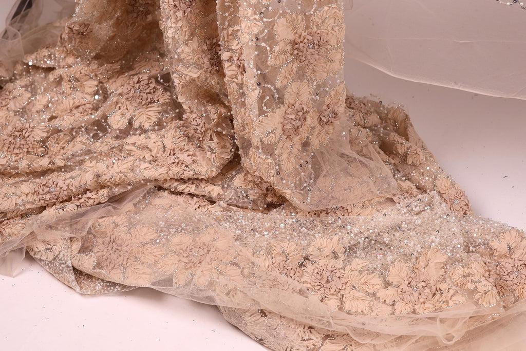 a close-up view of a delicate, beige-colored fabric with a floral pattern. The fabric appears to be made of sheer material, giving it a delicate and airy appearance.