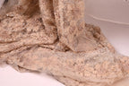 a close-up view of a delicate, beige-colored fabric with a floral pattern. The fabric appears to be made of sheer material, giving it a delicate and airy appearance.