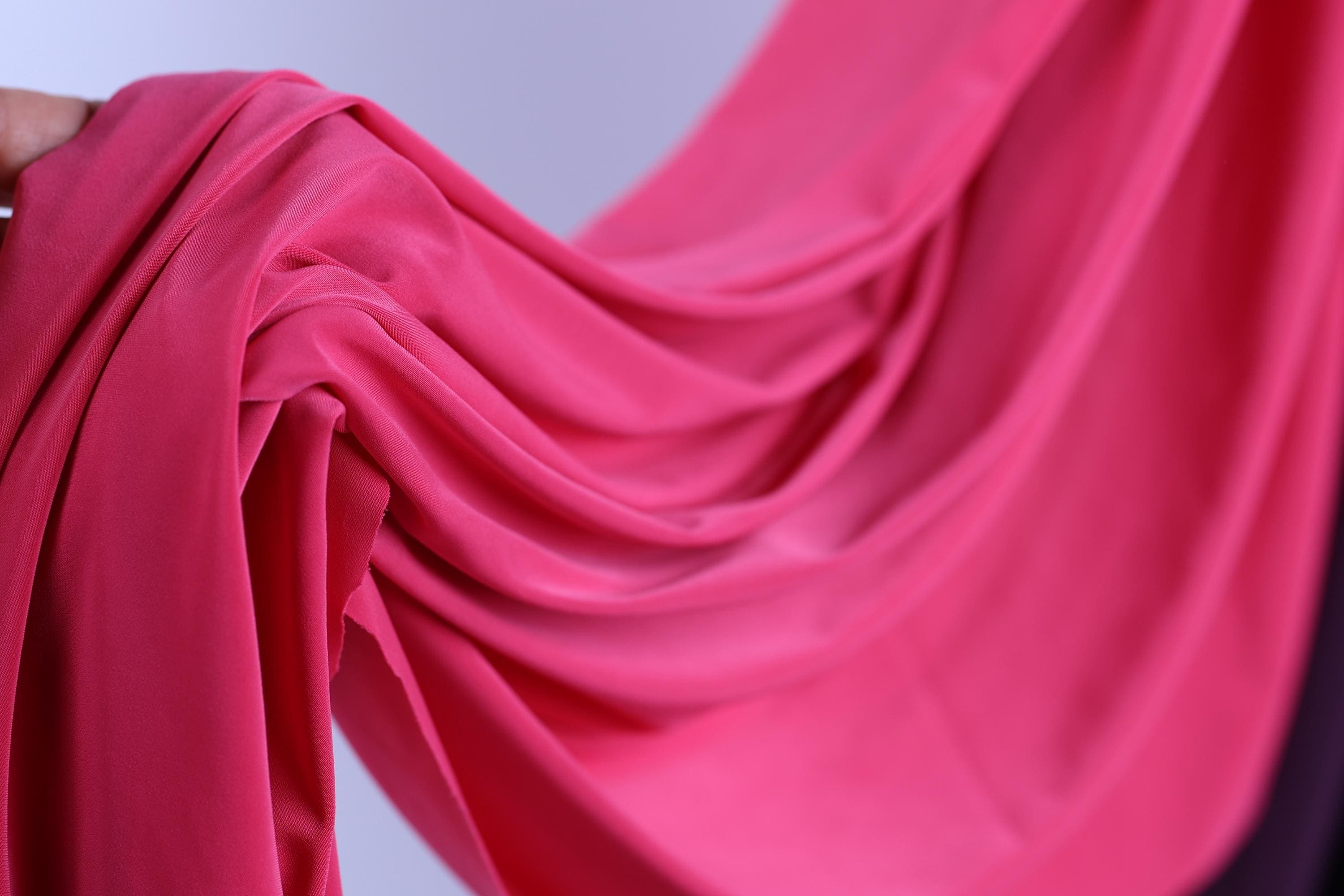 A close-up view of a vibrant pink fabric, possibly silk or chiffon, with a smooth, flowing texture.