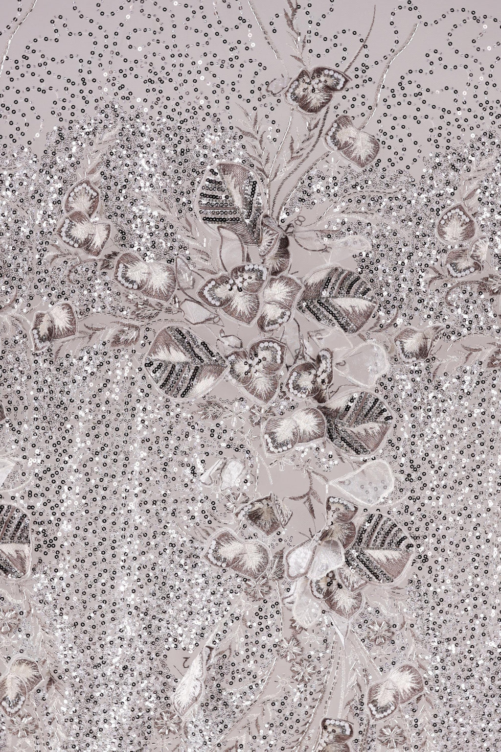 The image is a close-up of a fabric with a floral pattern, featuring a variety of small, intricately designed flowers and leaves. The fabric appears to be made of a shiny, metallic material, giving it a metallic, glittery appearance. The pattern is detailed and visually striking, with the flowers and leaves arranged in a way that creates a sense of depth and complexity.