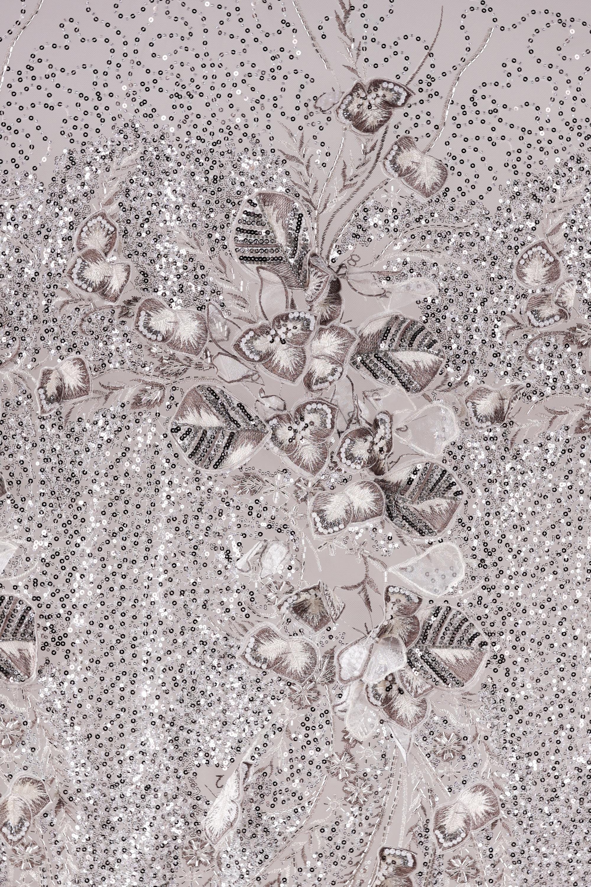 The image is a close-up of a fabric with a floral pattern, featuring a variety of small, intricately designed flowers and leaves. The fabric appears to be made of a shiny, metallic material, giving it a metallic, glittery appearance. The pattern is detailed and visually striking, with the flowers and leaves arranged in a way that creates a sense of depth and complexity.