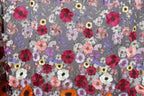 a close-up view of a fabric with a vibrant floral pattern. The fabric is adorned with a variety of colorful flowers, including red, pink, white, and yellow flowers, as well as purple and orange flowers. The flowers are intricately embroidered or sewn onto the fabric, creating a visually striking and detailed design. The image does not contain any text or other discernible objects, and the focus is solely on the floral pattern on the fabric.