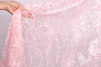 A hand is holding a piece of pink lace fabric with a floral pattern.
