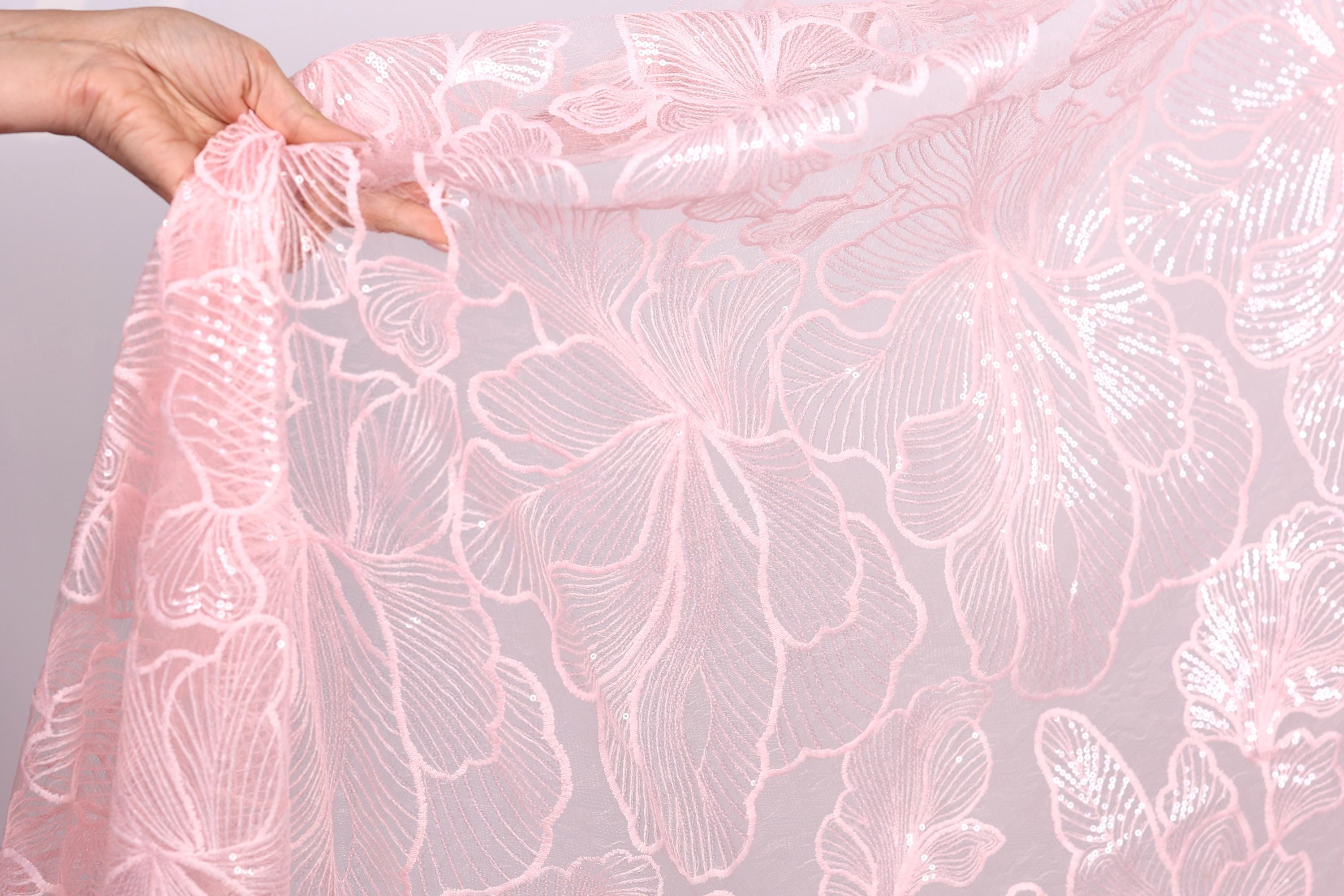 A hand is holding a piece of pink lace fabric with a floral pattern.