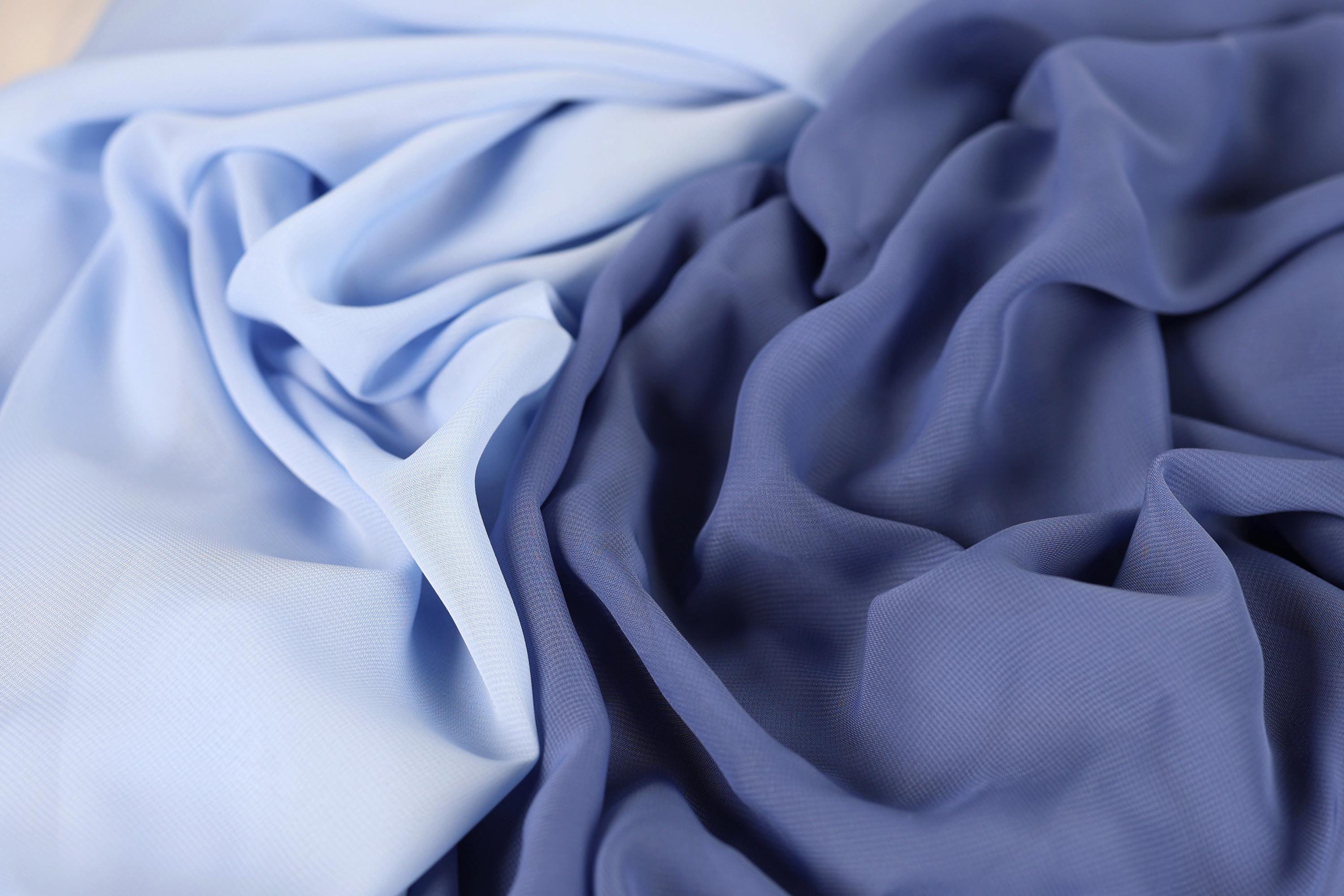 a close-up view of a fabric with a blue and white color gradient, featuring a mix of blue and white hues. The fabric appears to be crumpled and wrinkled, giving it a textured and soft appearance.