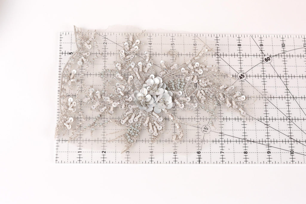 a delicate, intricate piece of lace or fabric adorned with a floral design, resting on a ruler or measuring mat.