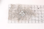a delicate, intricate piece of lace or fabric adorned with a floral design, resting on a ruler or measuring mat.