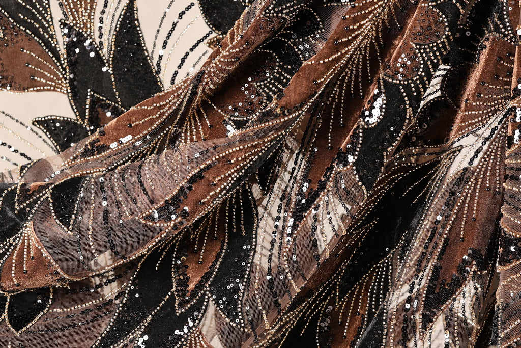 The image is a close-up of a fabric with a complex, intricate pattern of brown, black, and white sequins and beads. The pattern appears to be a mix of floral and geometric designs, creating a visually striking and detailed appearance.