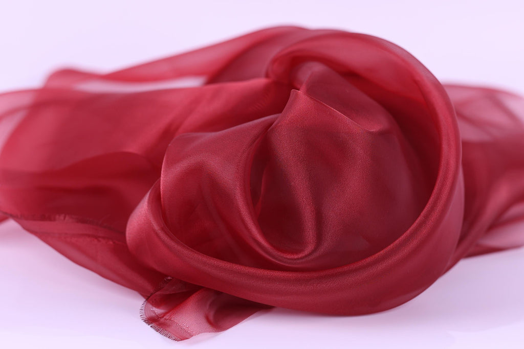 a close-up view of a red, flowing fabric, possibly silk or chiffon, with a soft, shiny texture.