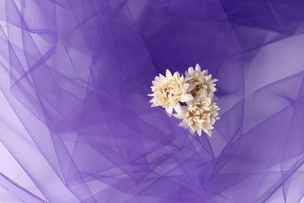 A delicate white flower rests on a soft purple fabric, creating a serene and elegant composition.