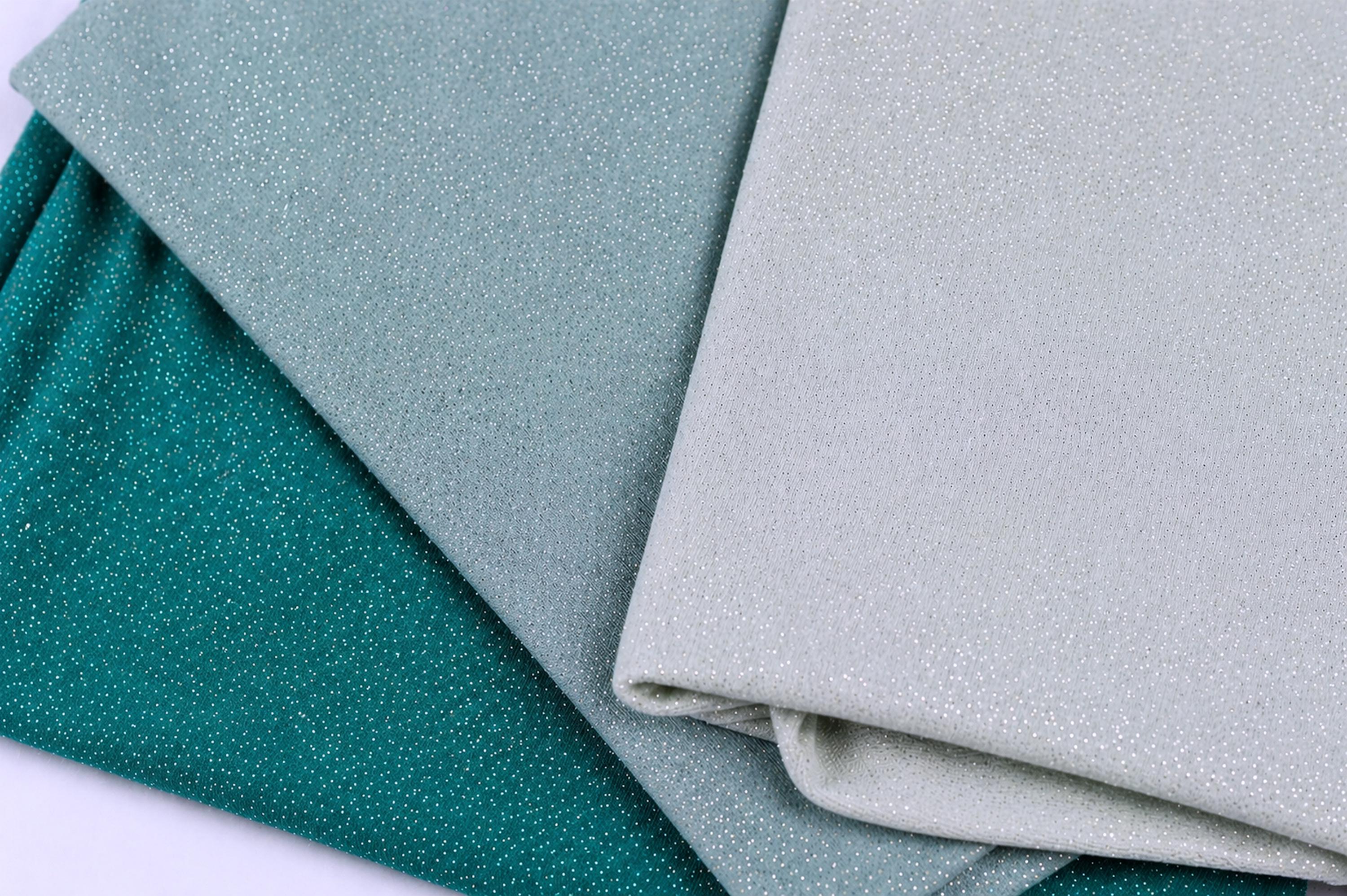 three fabric swatches, one in teal, one in light blue, and one in white, arranged on a surface.