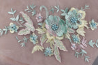 a close-up view of a delicate embroidered floral design on a fabric surface. The design includes various flowers and leaves, with the flowers being the main focus. The flowers are intricately crafted with beads, adding a touch of elegance and detail to the overall design. The arrangement of the flowers and leaves creates a visually appealing and harmonious composition.