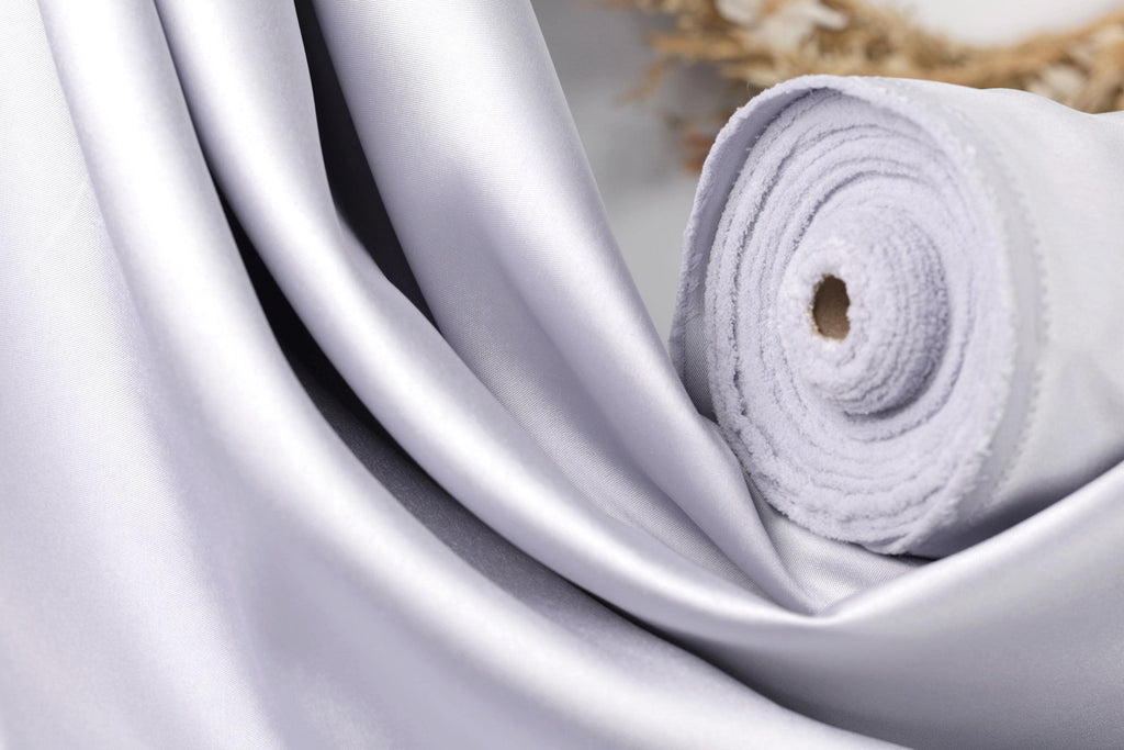 A close-up view of a white satin fabric, possibly silk, with a rolled-up end visible.