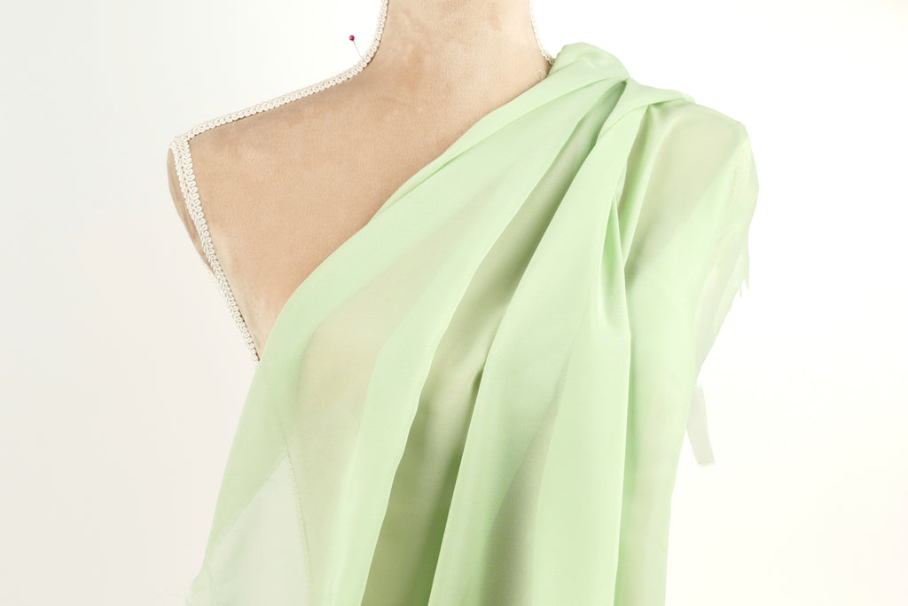 A mannequin wearing a green draped fabric draped over its shoulder.