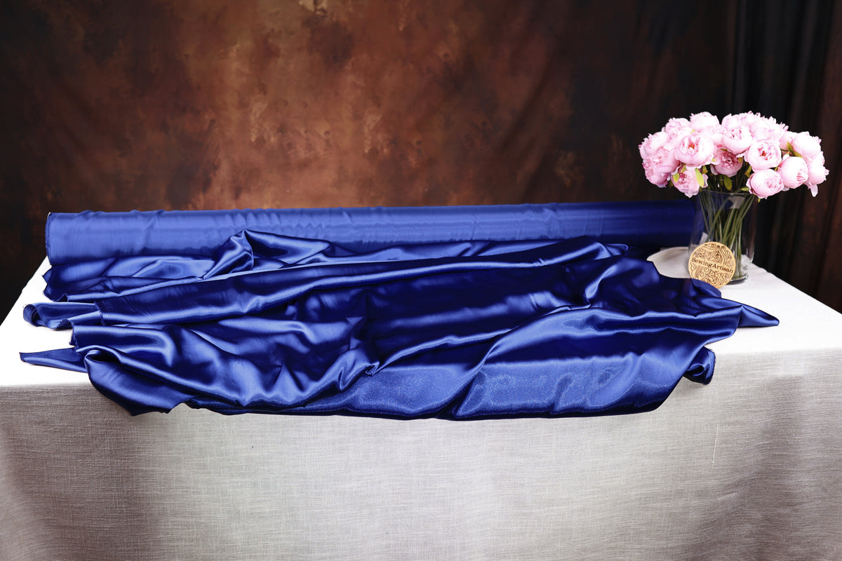 a table with a blue satin fabric draped over it, and a vase of pink flowers placed on the table.