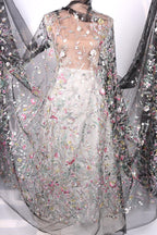 a dress with a sheer, floral-patterned fabric. The dress appears to be made of sheer material, giving it a delicate and elegant appearance. The dress is adorned with a variety of flowers and leaves, creating a visually striking and intricate design. The dress is displayed on a mannequin, showcasing its unique and eye-catching design.