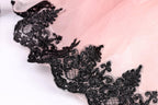 A close-up view of a delicate, lace-like fabric with a pink background and black lace trim.