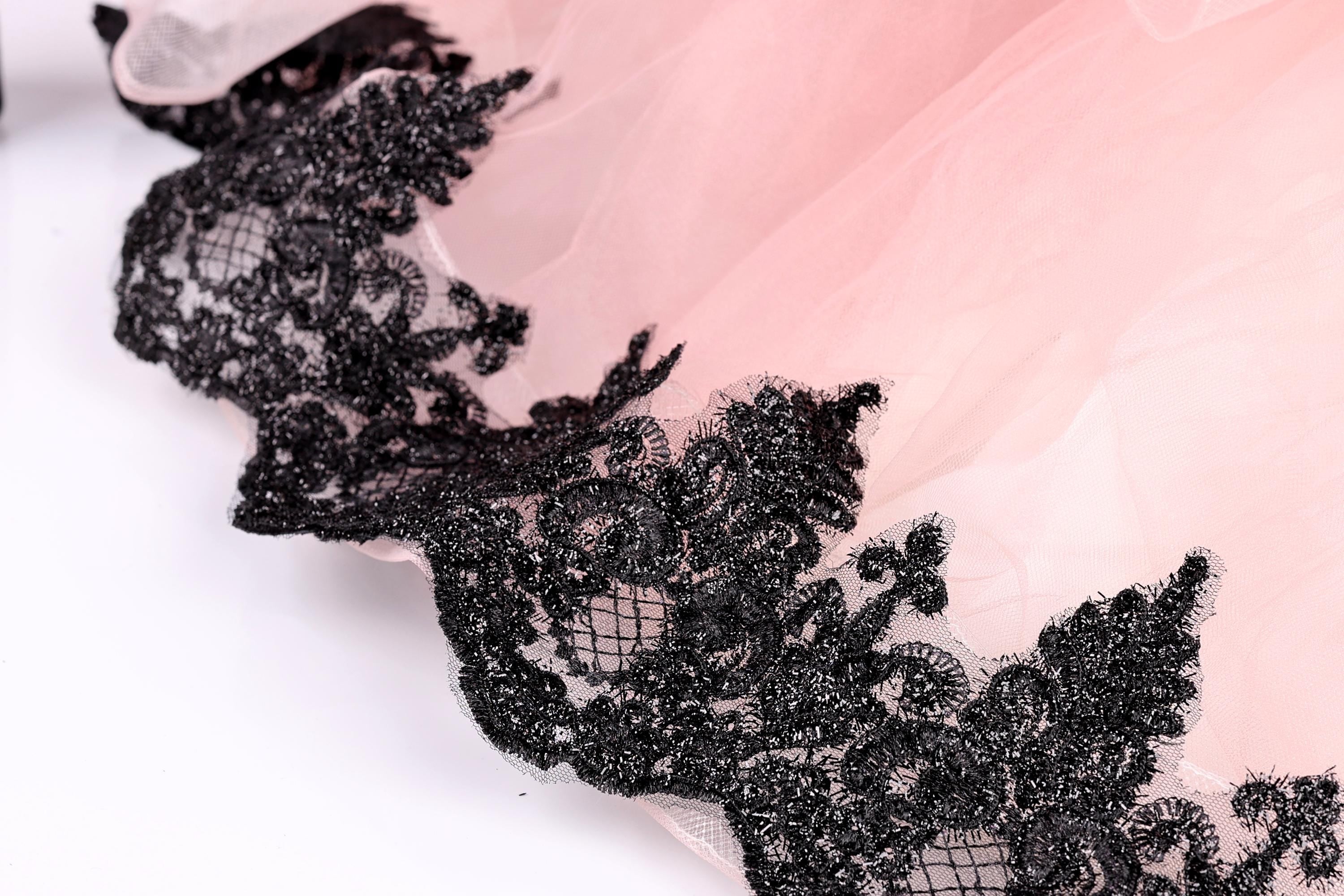 A close-up view of a delicate, lace-like fabric with a pink background and black lace trim.