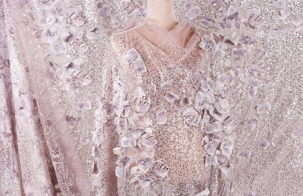 a mannequin wearing a dress with a delicate, intricate floral pattern. The dress is predominantly pink and white, with the floral design being the most prominent element. The mannequin is positioned in the center of the image, showcasing the dress and its details.