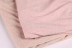 a close-up view of a fabric with a metallic, glittery texture. The fabric appears to be a light pink color, and it is folded or crumpled, creating a sense of depth and texture.