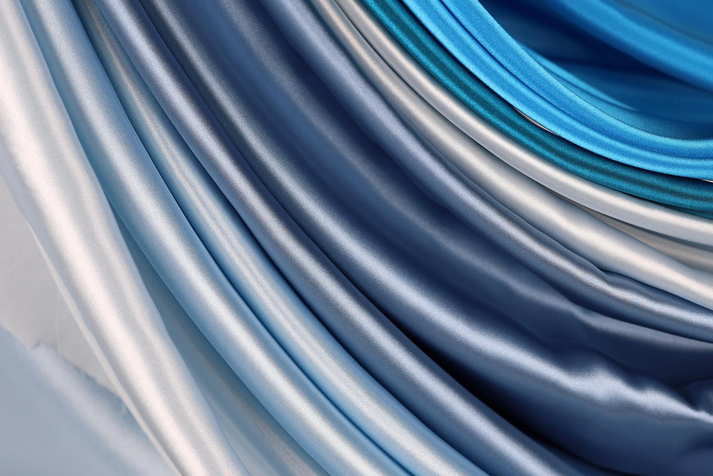 a close-up view of a collection of blue and silver satin fabric, with the fabric appearing to be folded or draped in a cascading manner.