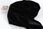 a black velvet fabric with a glittery texture, placed on a white surface next to a clear plastic container filled with colorful pins.