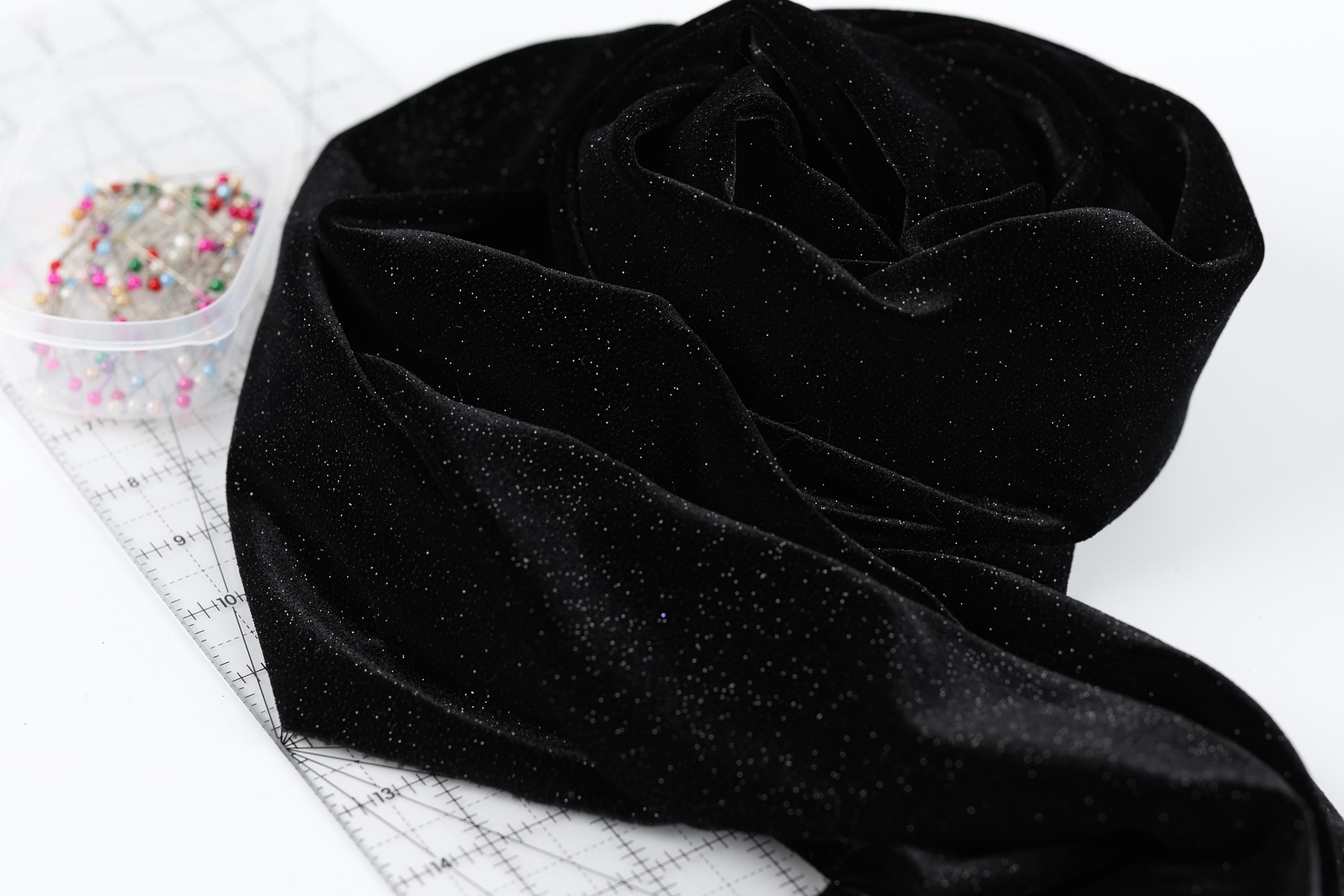 a black velvet fabric with a glittery texture, placed on a white surface next to a clear plastic container filled with colorful pins.