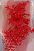 a close-up view of a red floral embroidered design on a fabric, with a pink background.