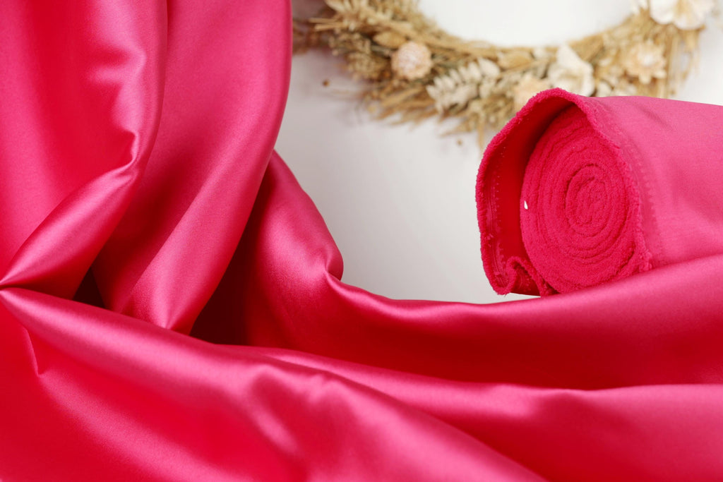 a close-up view of a vibrant red satin fabric, with a wreath of dried flowers in the background.