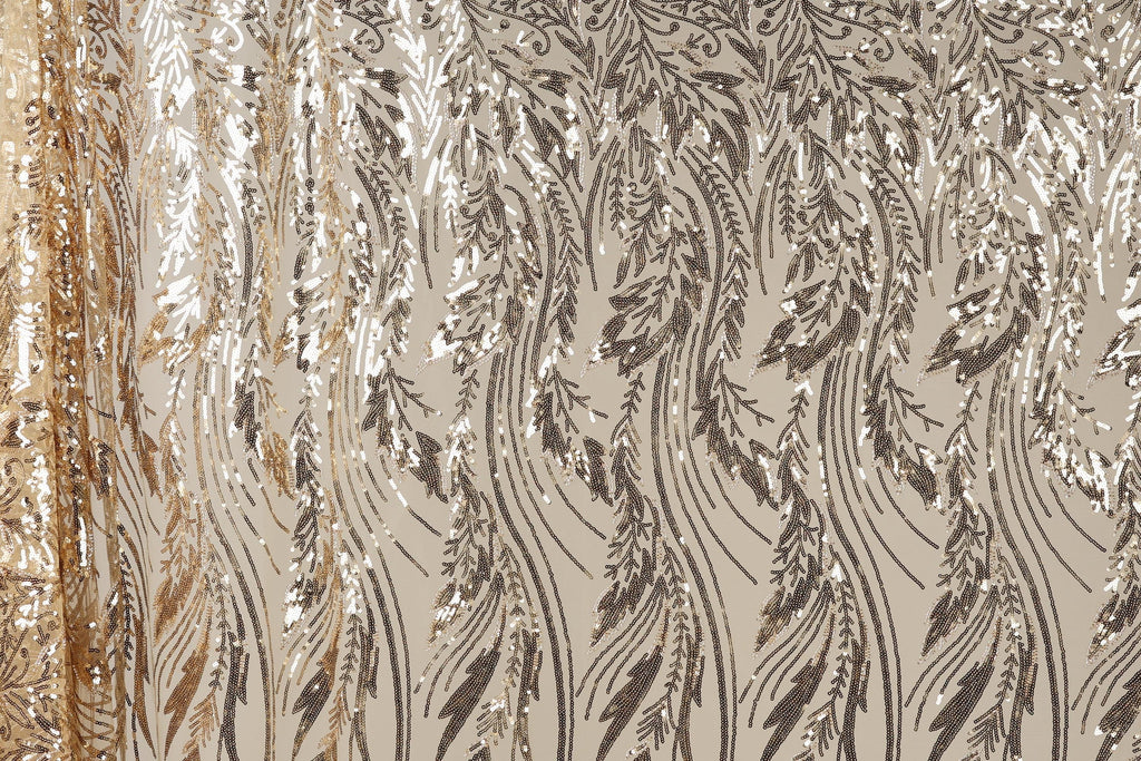 a close-up view of a fabric with a repeating pattern of sequin designs in shades of brown and gold. The pattern appears to be a floral or leaf-like design, with the sequins arranged in a way that creates a sense of movement and texture. The fabric has a shiny, metallic appearance, which adds to the overall visual appeal of the image.