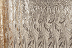 a close-up view of a fabric with a repeating pattern of sequin designs in shades of brown and gold. The pattern appears to be a floral or leaf-like design, with the sequins arranged in a way that creates a sense of movement and texture. The fabric has a shiny, metallic appearance, which adds to the overall visual appeal of the image.
