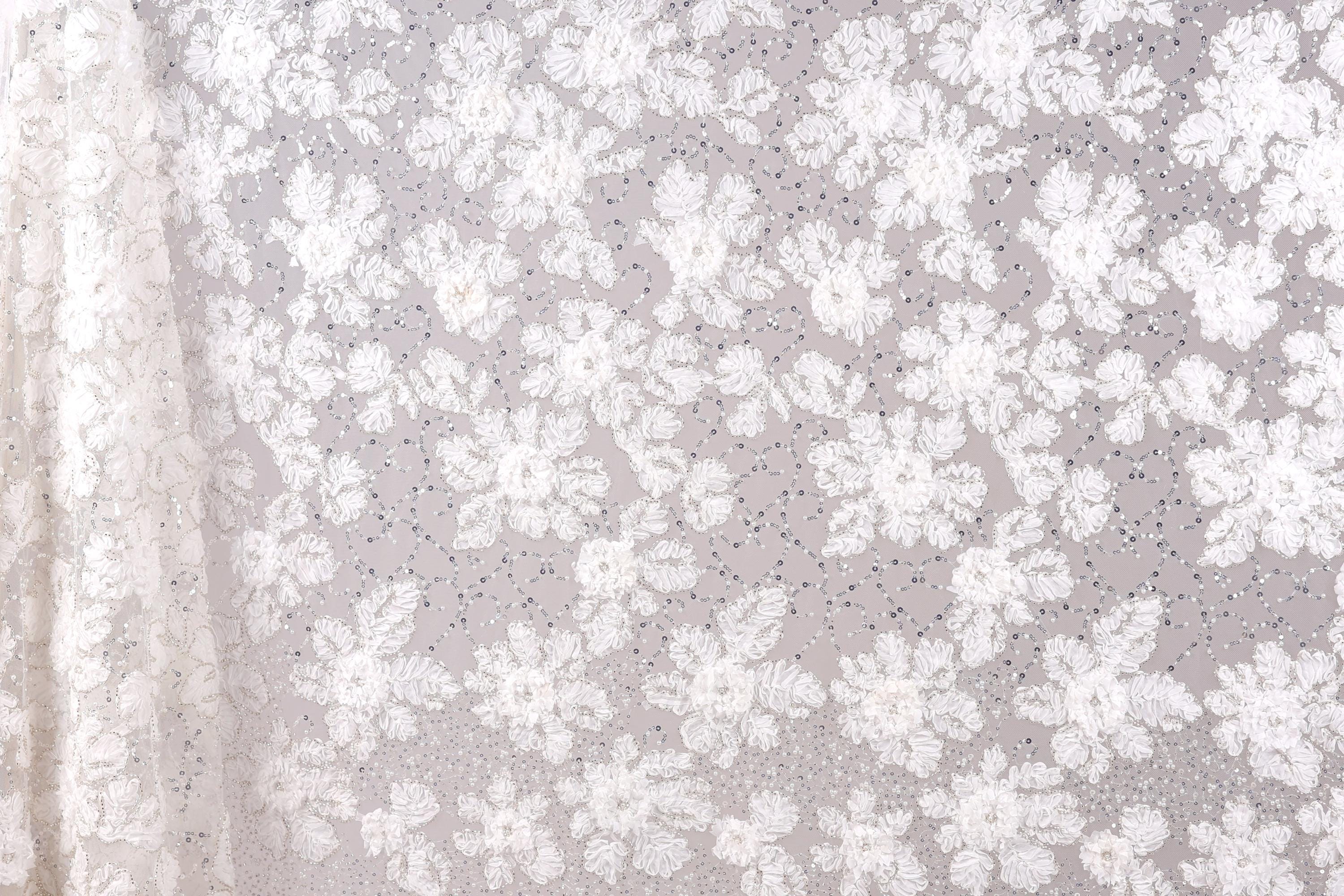 a close-up view of a delicate, white lace fabric with a floral pattern. The fabric appears to be made of sheer material, giving it a delicate and elegant appearance. The lace fabric is spread across the entire image, creating a sense of depth and texture. The floral pattern on the fabric is intricate and detailed, showcasing the craftsmanship and artistry involved in creating such a piece of textile art.