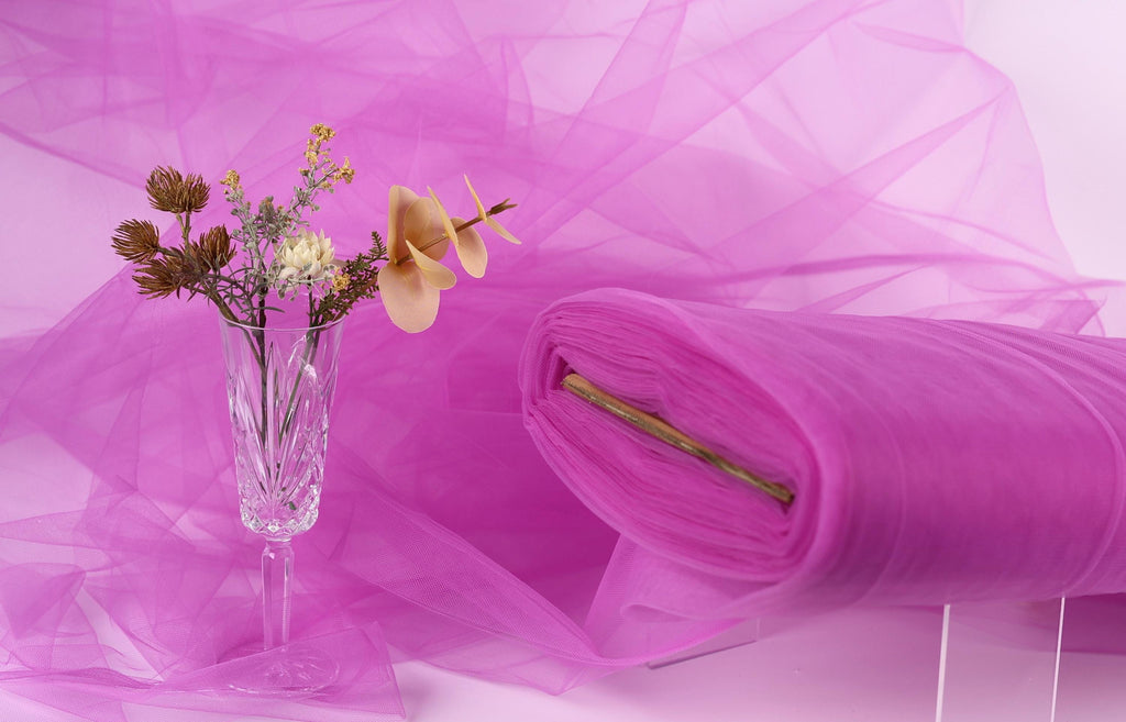a clear glass vase holding a bouquet of flowers, placed on a pink background.