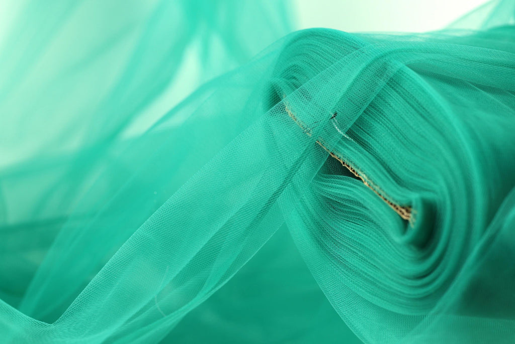 A close-up view of a roll of turquoise-colored fabric, with a blurred background.