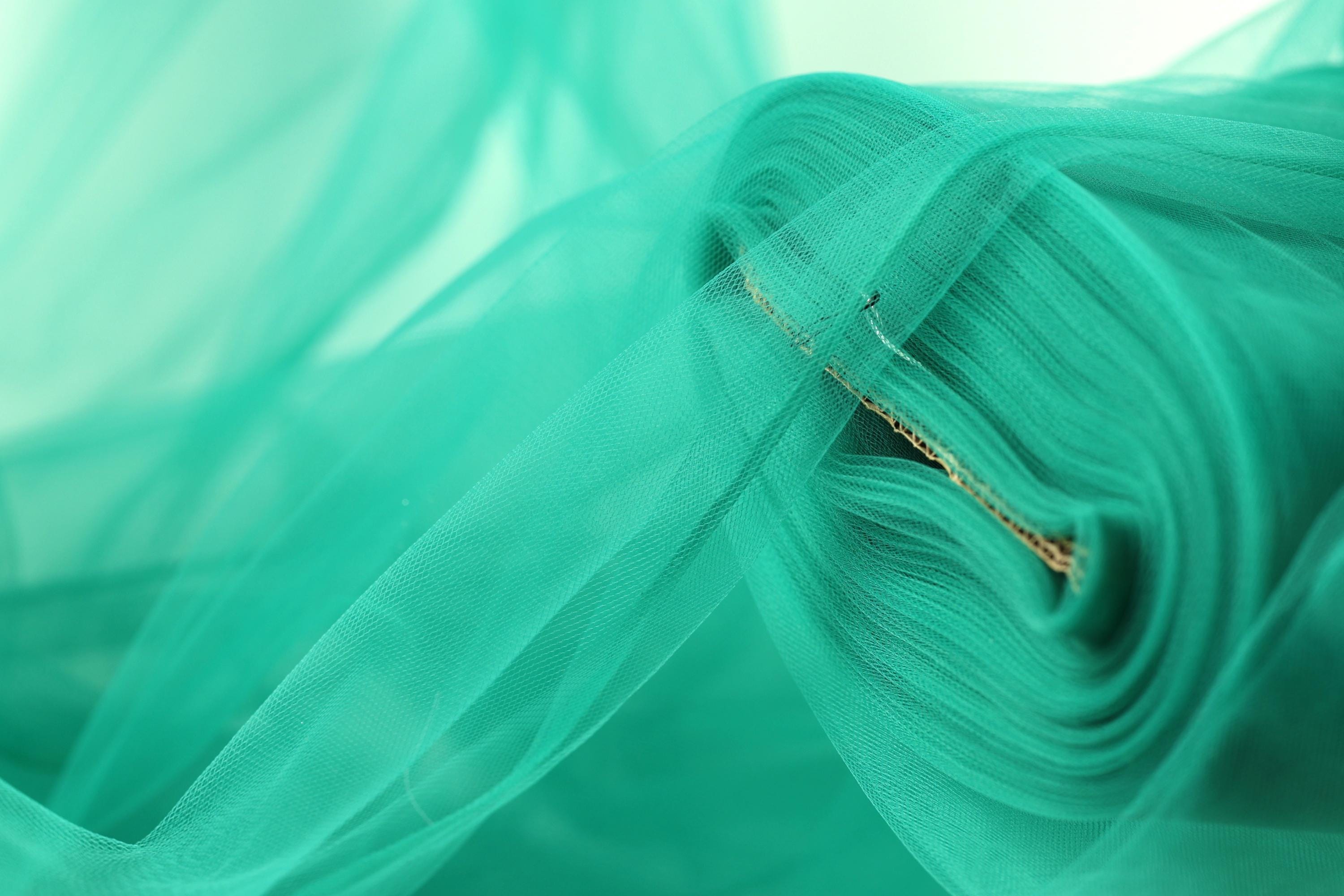 A close-up view of a roll of turquoise-colored fabric, with a blurred background.