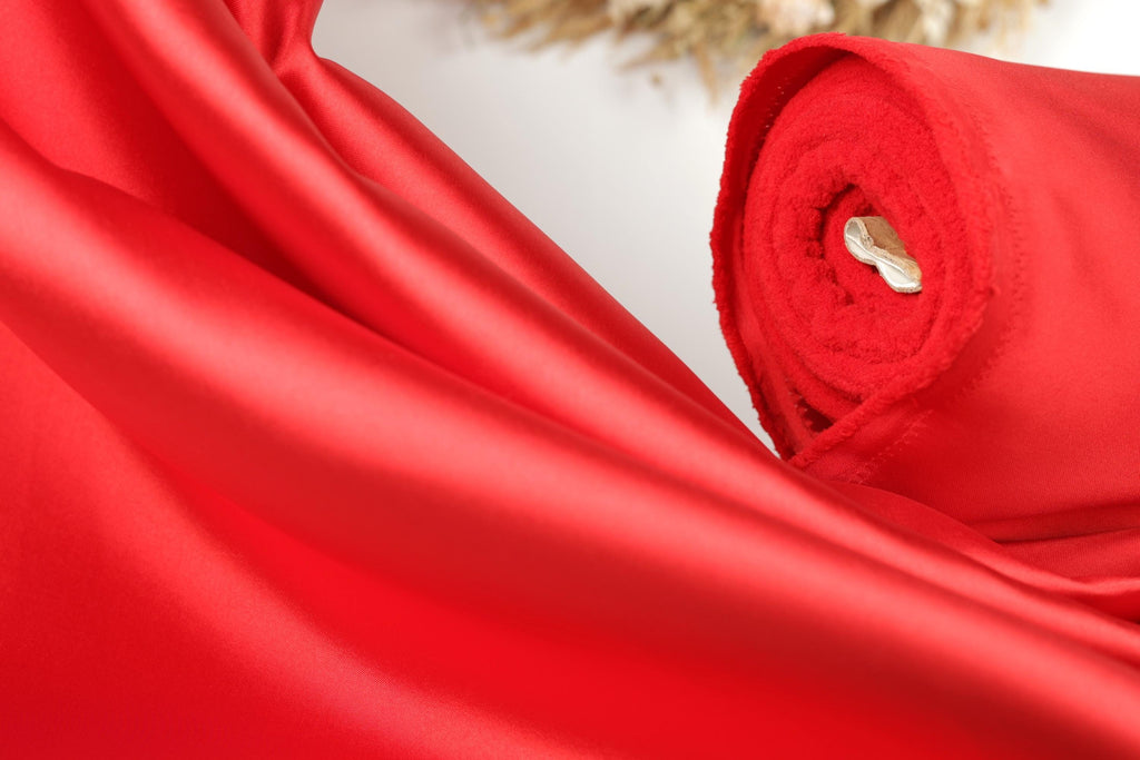 A close-up view of a vibrant red fabric, possibly silk or satin, with a white object visible in the center.