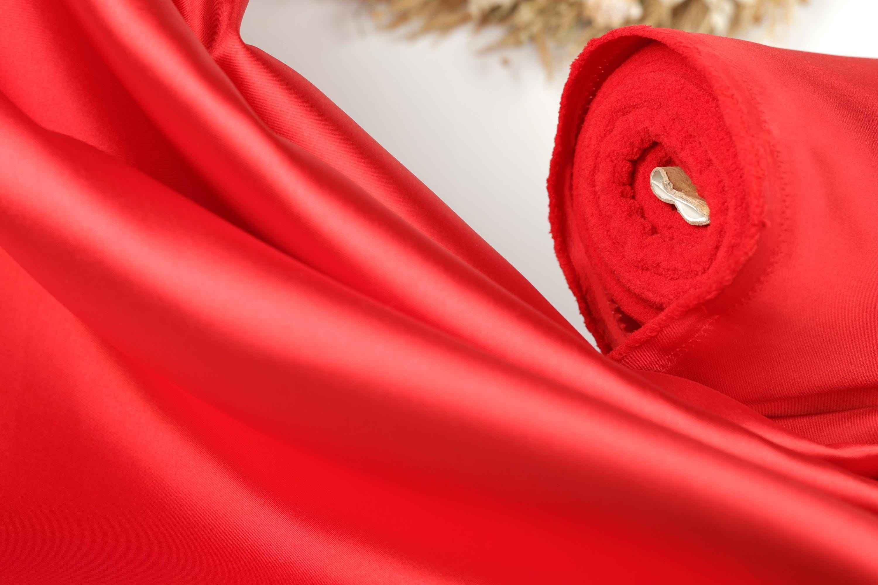 A close-up view of a vibrant red fabric, possibly silk or satin, with a white object visible in the center.