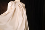 A flowing, draped fabric in a pale color, possibly white or light pink, is displayed against a dark background.
