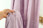 A hand is holding a folded purple fabric in front of a curtain.