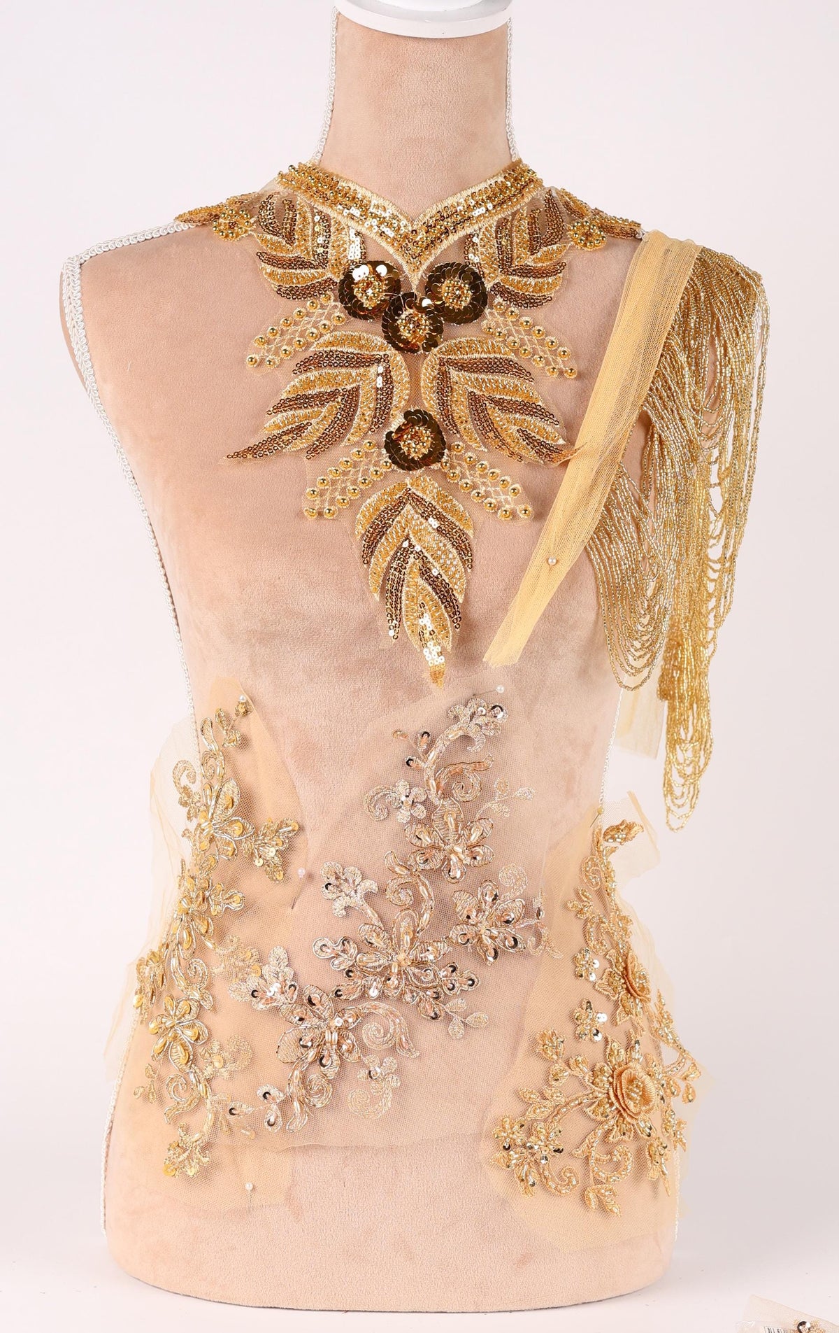 A mannequin wearing an elaborate gold and beige dress with intricate embroidery and embellishments.