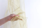 A hand is holding a piece of gold glittery fabric against a white background.