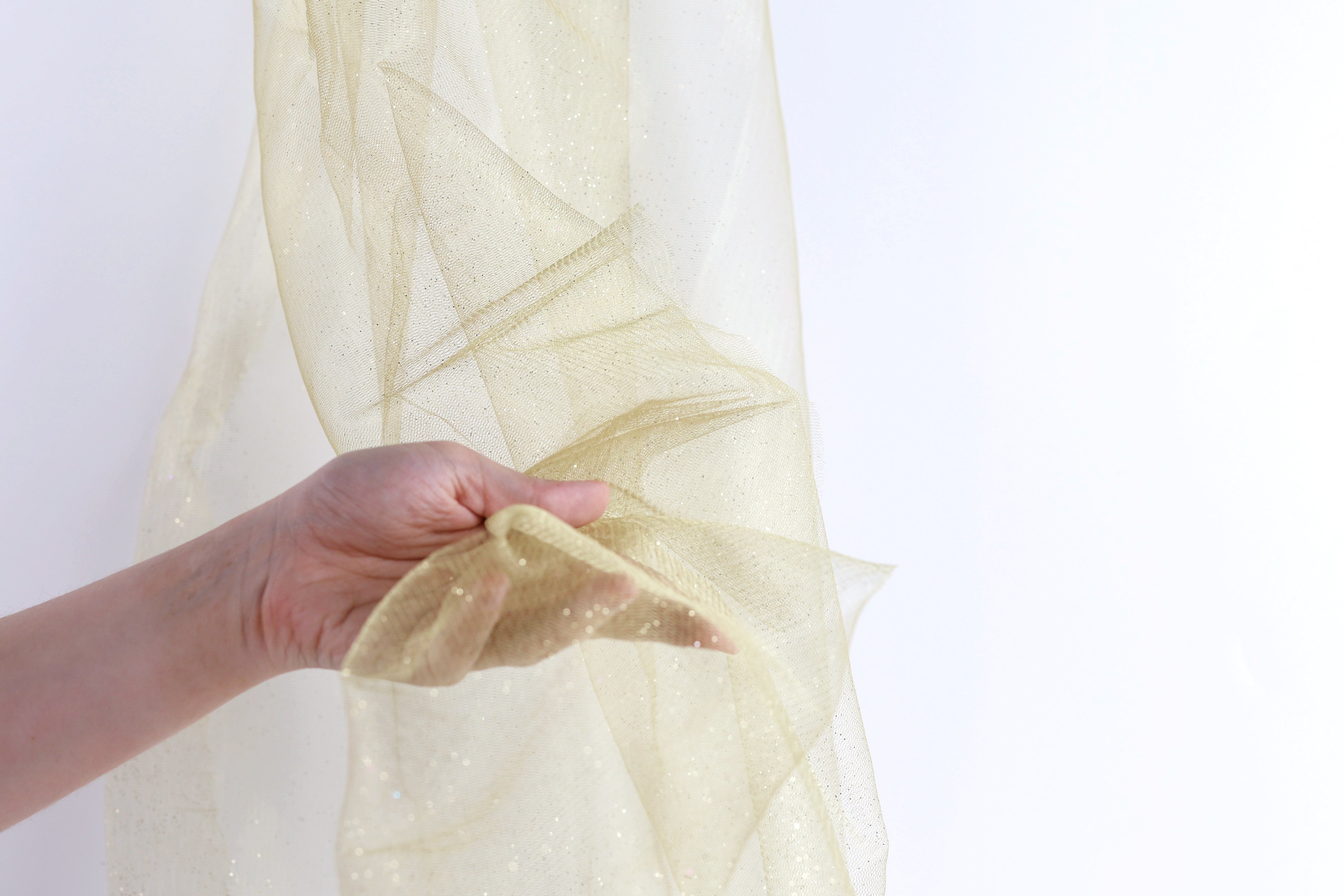 A hand is holding a piece of gold glittery fabric against a white background.