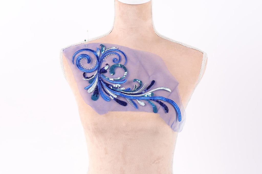 a mannequin with a decorative piece of fabric on its chest. The fabric is adorned with a blue and purple floral design, which appears to be a handmade embroidery or appliqué.