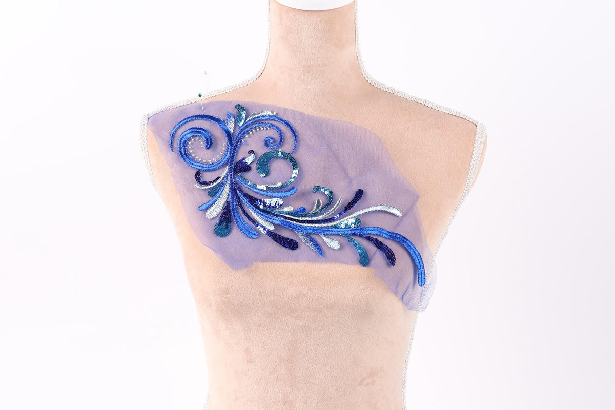 a mannequin with a decorative piece of fabric on its chest. The fabric is adorned with a blue and purple floral design, which appears to be a handmade embroidery or appliqué.