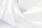 The image is a close-up of a soft, white fabric, possibly silk or satin, with a smooth and flowing texture.
