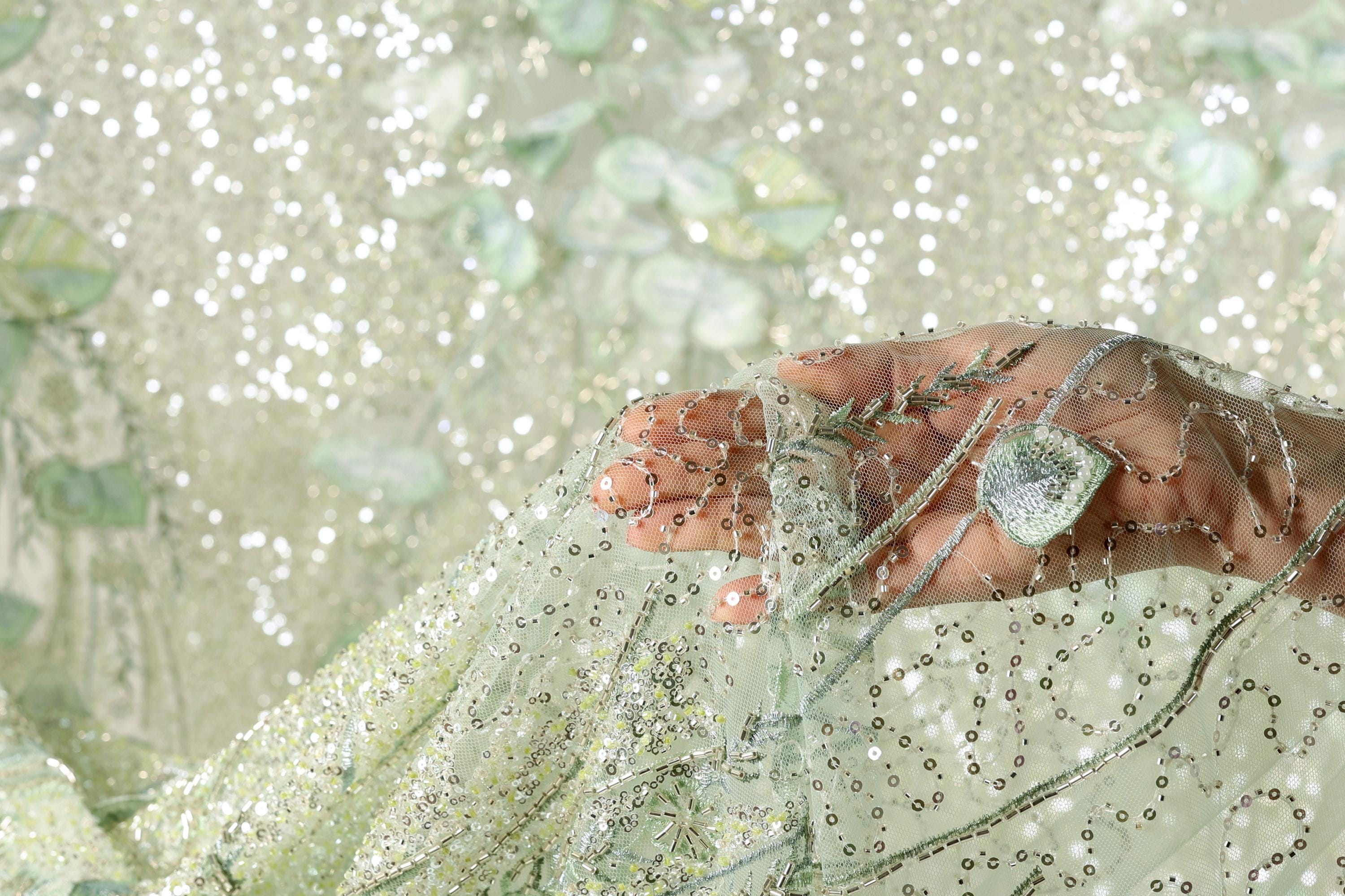A hand is holding a piece of fabric with a floral pattern, and the background is a light green color with small white dots.