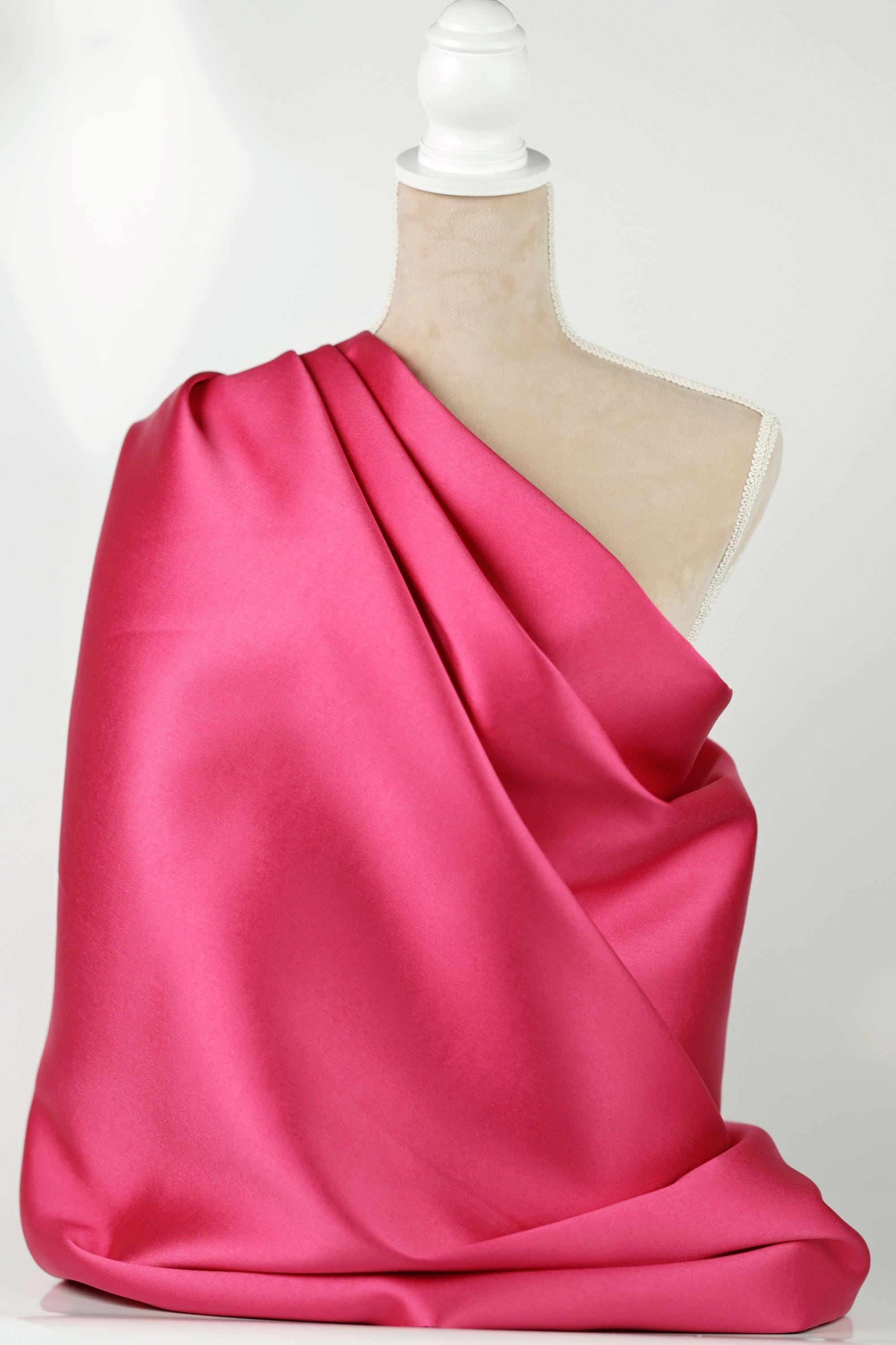 A mannequin is wearing a bright pink satin fabric draped over its body.