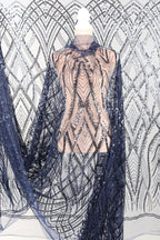 a mannequin wearing a dress with a sheer, sequined bodice and a long, flowing cape. The cape has a black and silver pattern, and the dress appears to be made of a sheer fabric with a metallic, sequined effect.