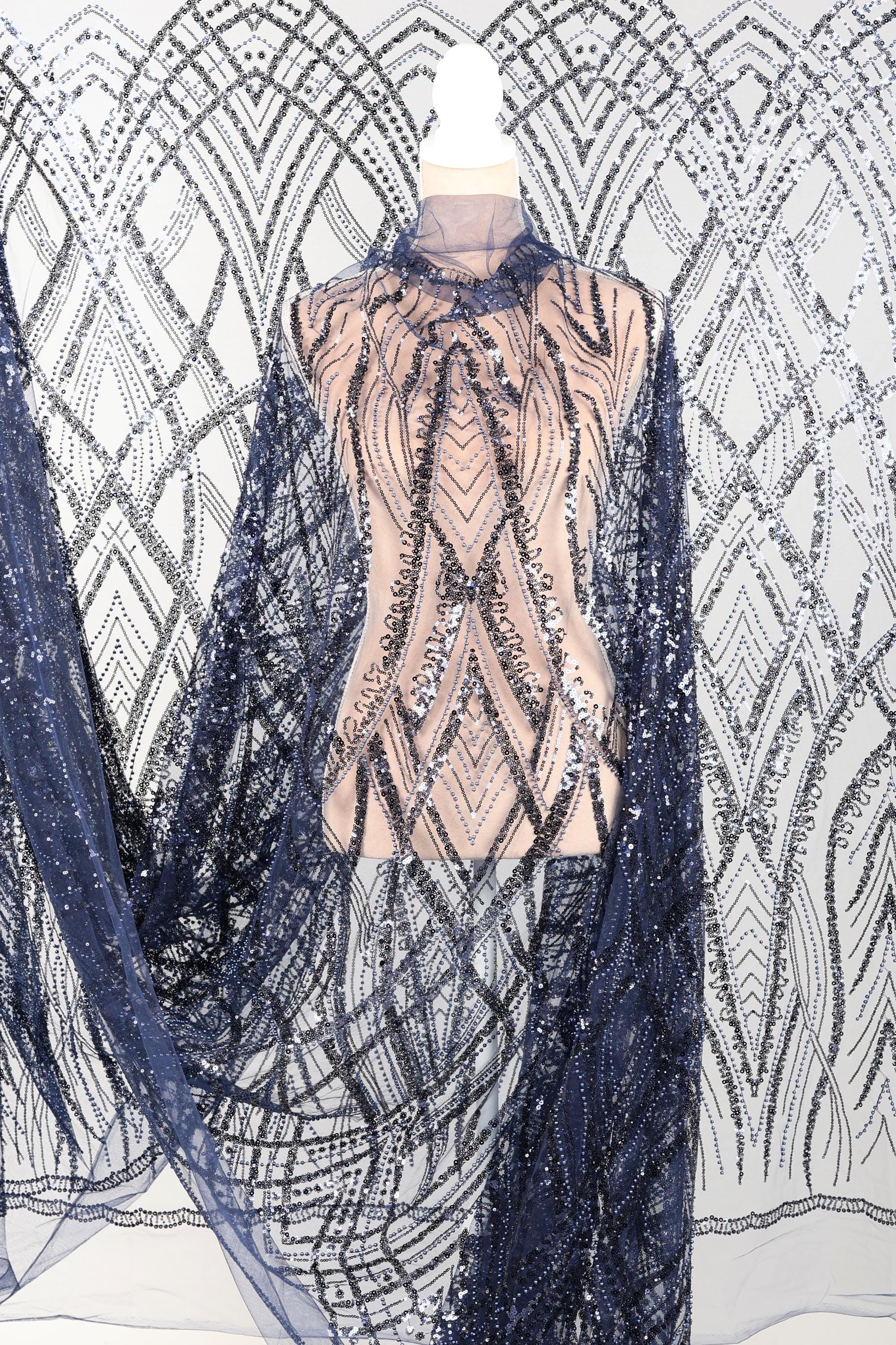 a mannequin wearing a dress with a sheer, sequined bodice and a long, flowing cape. The cape has a black and silver pattern, and the dress appears to be made of a sheer fabric with a metallic, sequined effect.