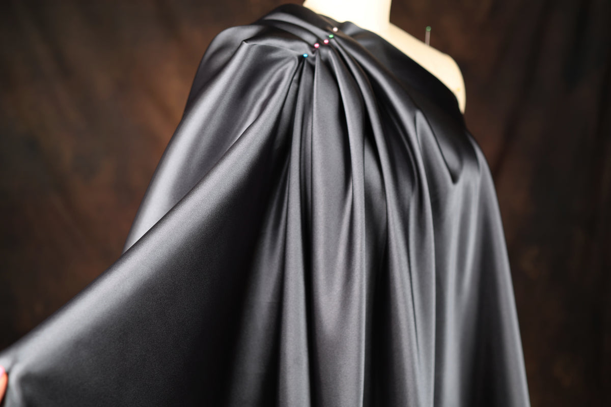A close-up view of a black satin garment with a draped, flowing design.